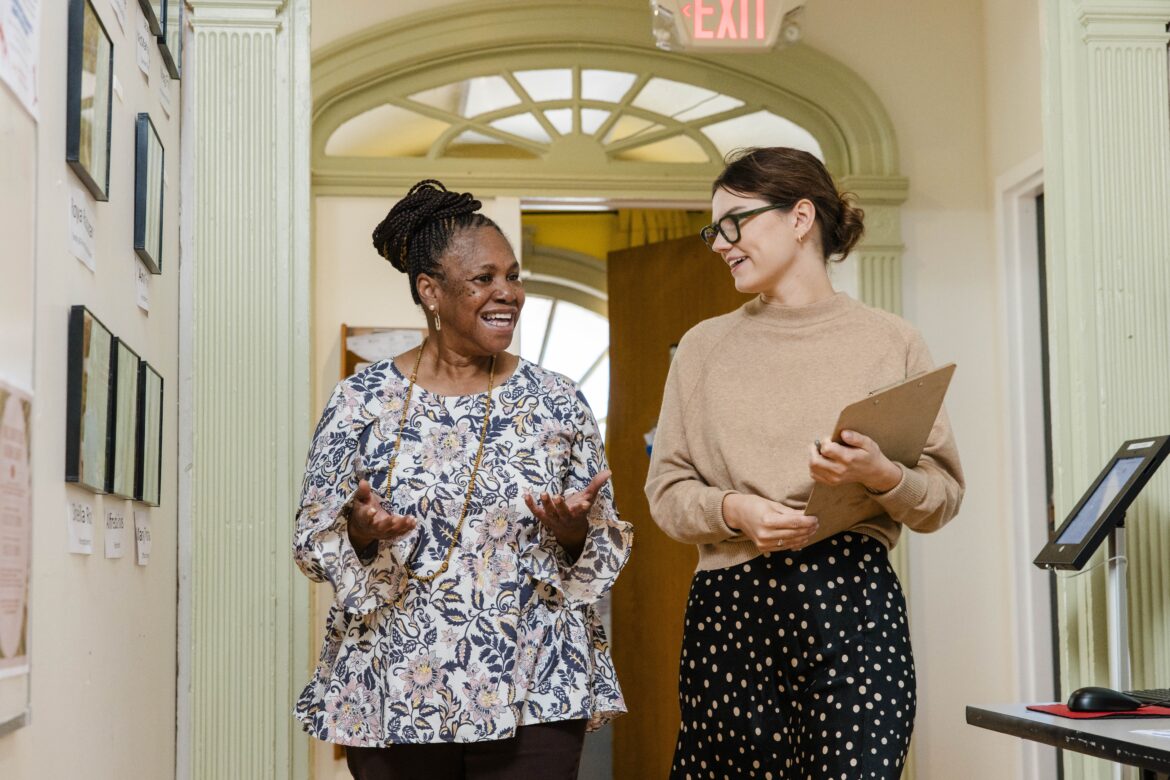 Two people walk through a hallway as they have a conversation.