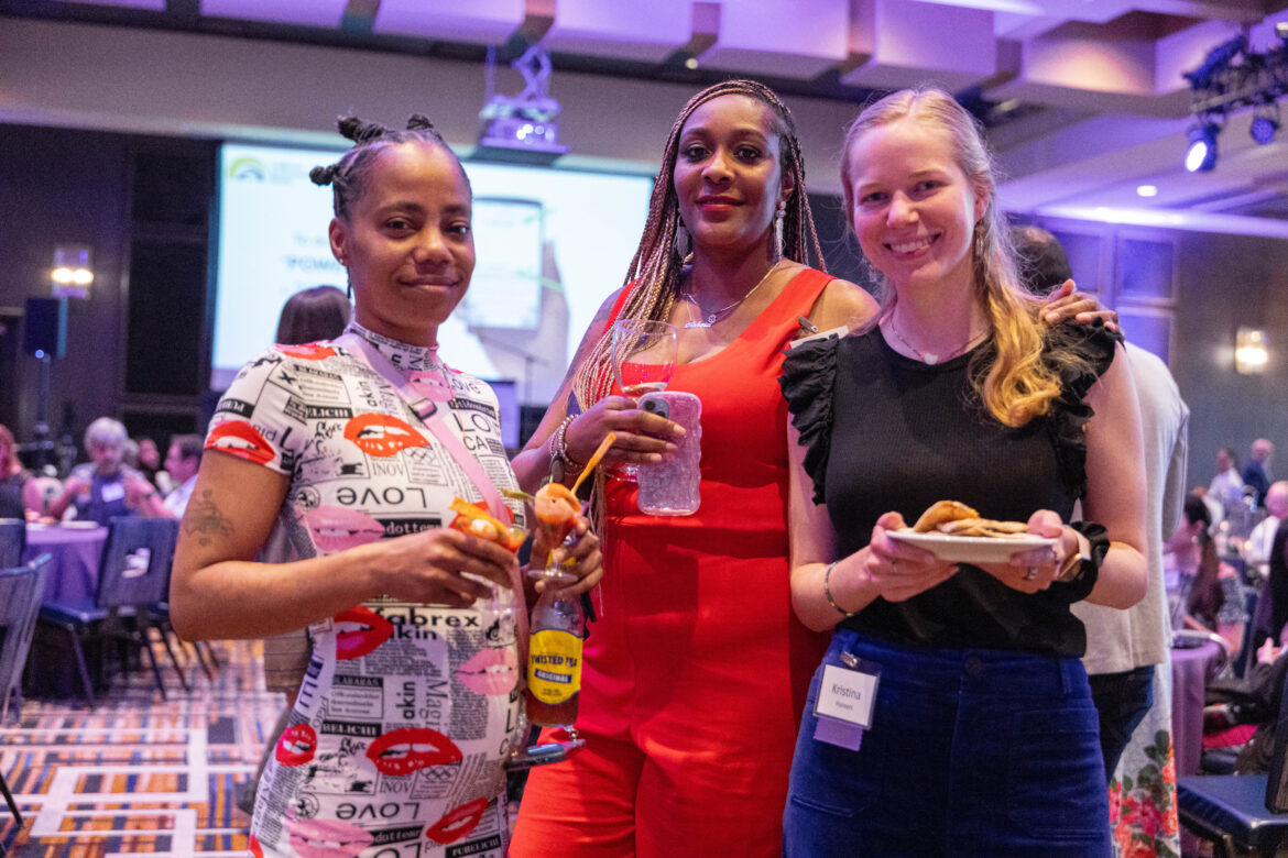 Three women holding food and drinks smile for the camera