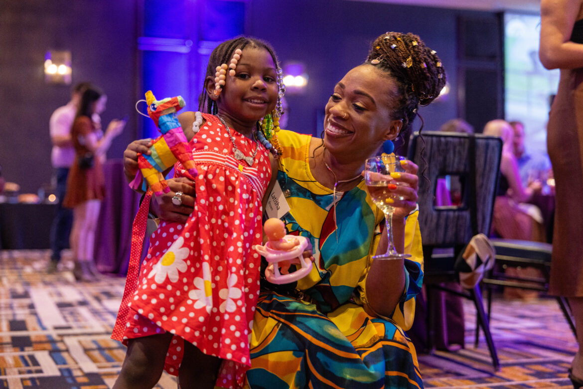 A smiling woman poses with her arm around a little girl